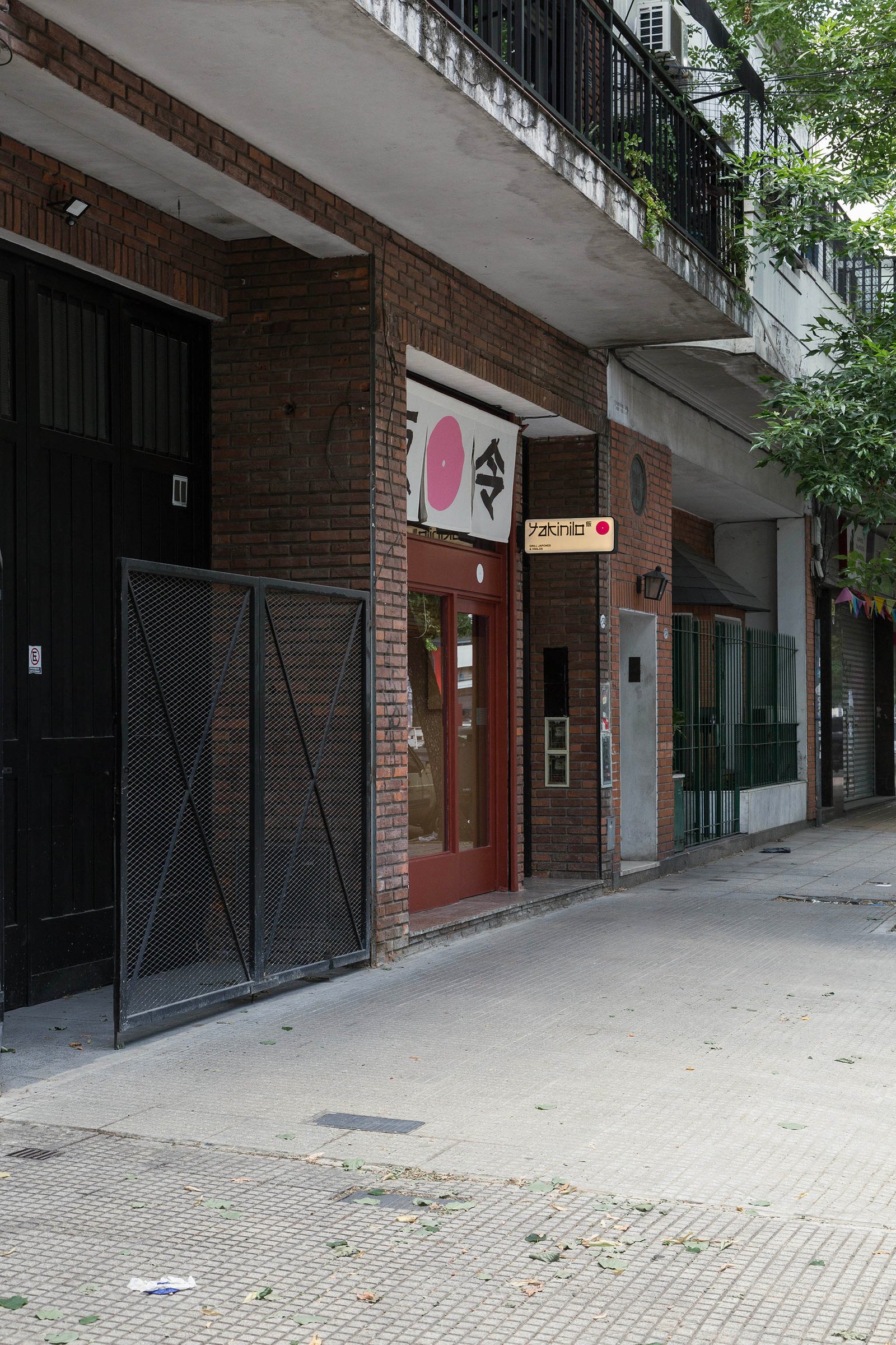 Fachada comercial de tijolos com porta vermelha e placa japonesa — projeto Yakinilo, por Estudio YME, em Av. Dorrego 1551